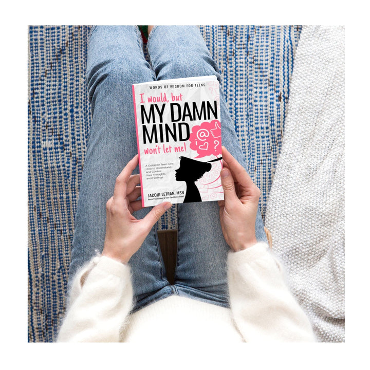 Top edge of the paperback teen girl book showing textured purple cover with subtle embossed title details and a glimpse of