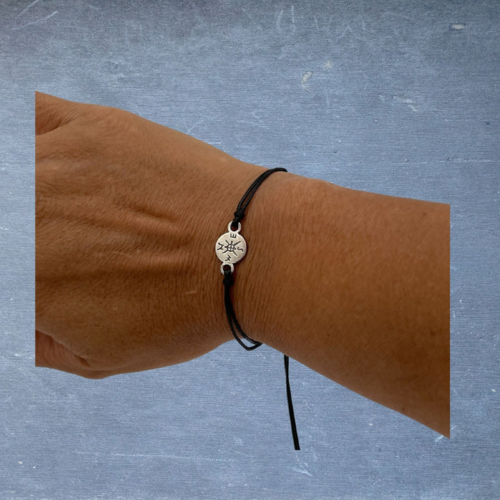 Close-up of the Pinky Promise Bracelet's sterling silver compass charm with engraved detailing, showcasing intricate